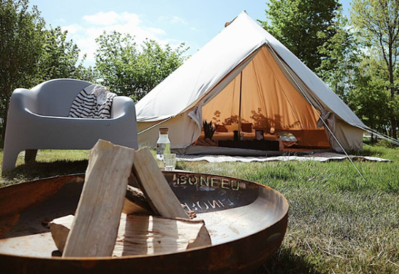 Foto eines Bell Tent 500 Safari-Zeltes mit offener Tür, Feuerschale und Sitzgelegenheit im Grünen.