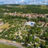 Aerial view of Camping Le Château holiday park in Auvergne-Rhône-Alpes, France, with green trees and pools.