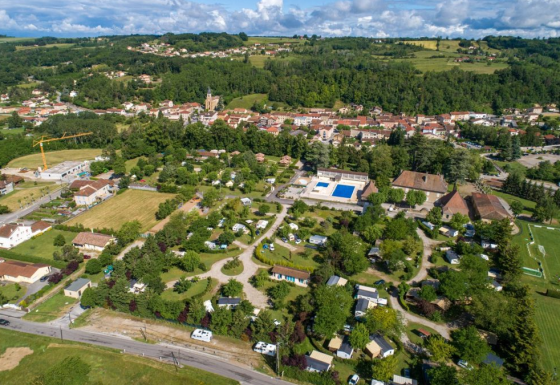 Aerial view of Camping Le Château holiday park in Auvergne-Rhône-Alpes, France, with green trees and pools.