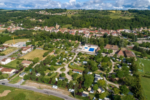 Aerial view of Camping Le Château holiday park in Auvergne-Rhône-Alpes, France, with green trees and pools.
