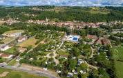 Vista aérea del camping Le Château en Auvergne-Rhône-Alpes, Francia, rodeado de árboles y piscinas azules.