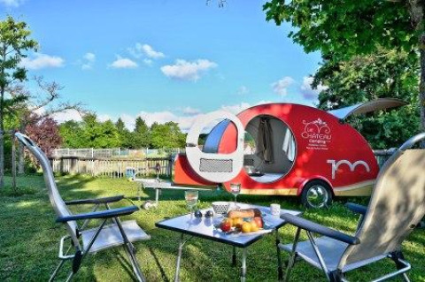 Escena al aire libre en Camping Le Château en Auvergne-Rhône-Alpes, Francia, con caravana y mesa de picnic.