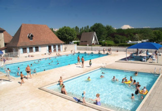 Outdoor pools at Camping Le Château, Auvergne-Rhône-Alpes, France, with families relaxing and swimming.
