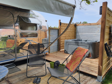 Terrasse mit Liegestühlen und Whirlpool neben einem Wohnwagen im Camping Le Château, Auvergne-Rhône-Alpes.