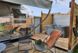Terrasse mit Liegestühlen und Whirlpool neben einem Wohnwagen im Camping Le Château, Auvergne-Rhône-Alpes.