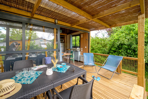 Überdachte Terrasse mit Esstisch und Liegestühlen im Camping Le Château, Auvergne-Rhône-Alpes, Frankreich.