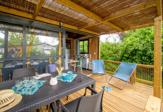 Überdachte Terrasse mit Esstisch und Liegestühlen im Camping Le Château, Auvergne-Rhône-Alpes, Frankreich.