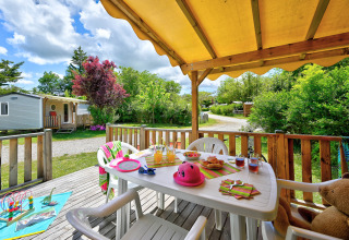 Terrazza soleggiata con tavolo, sedie e giocattoli al Camping Le Château, Auvergne-Rhône-Alpes, Francia.