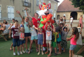 Children and adults pose with a fox mascot at Camping Le Château, a holiday park in Auvergne-Rhône-Alpes, France.