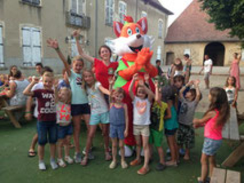 Børn og voksne smiler og vinker foran et stort ræv-maskot ved Camping Le Château i Auvergne-Rhône-Alpes.