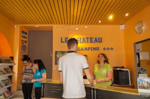 Recepción en Camping Le Château con personal y huéspedes en el parque vacacional de Auvergne-Rhône-Alpes, Francia.