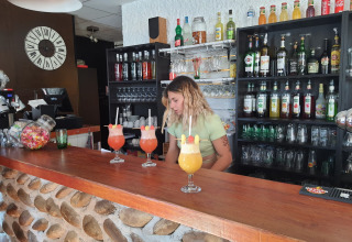 Bartender preparing colorful cocktails behind the bar at Camping Le Château, Auvergne-Rhône-Alpes, France.