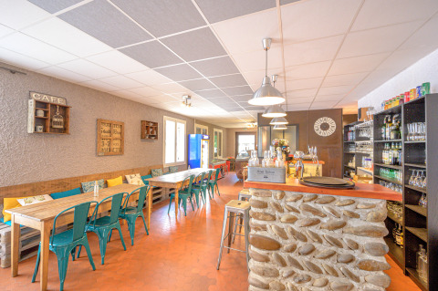 Helles Café im Camping Le Château, Auvergne-Rhône-Alpes, Frankreich, mit Steinbar und modernen Sitzgelegenheiten.