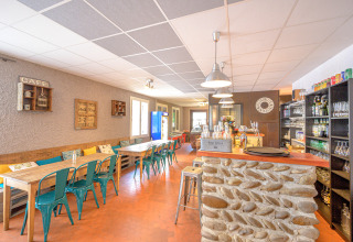 Bright, cozy café area at Camping Le Château, Auvergne-Rhône-Alpes, France, with stone bar and wooden tables.