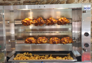 Polli allo spiedo e patate che cuociono in un forno commerciale al Camping Le Château in Francia.