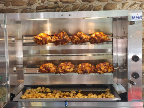 Pollos rostizados y papas cocinándose en un asador comercial en Camping Le Château en Francia.
