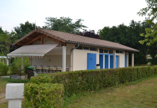 Gebouw met blauwe deuren en buitenwasbakken op Camping Le Château in Auvergne-Rhône-Alpes, Frankrijk.