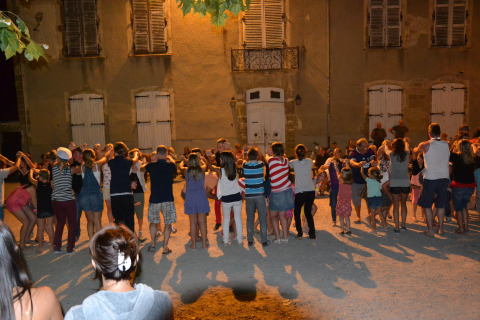 Gruppo di persone che ballano e giocano insieme di sera davanti a un edificio al Camping Le Château, Francia.