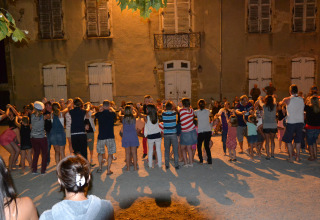 Gruppo di persone che ballano e giocano insieme di sera davanti a un edificio al Camping Le Château, Francia.
