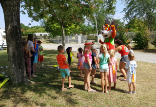 Children gather around a mascot under trees at Camping Le Château holiday park, Auvergne-Rhône-Alpes, France.