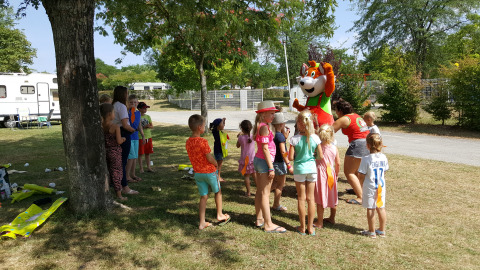 Niños reunidos alrededor de una mascota bajo los árboles en Camping Le Château, Auvergne-Rhône-Alpes, Francia.