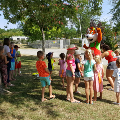 Bambini si radunano attorno a una mascotte sotto gli alberi a Camping Le Château, Auvergne-Rhône-Alpes, Francia.
