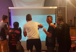 Fünf Menschen singen Karaoke vor einem Projektor im Camping Le Château, Auvergne-Rhône-Alpes, Frankreich.