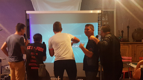 Cinco personas cantan karaoke frente a una pantalla en Camping Le Château, Auvergne-Rhône-Alpes, Francia.