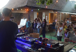 Outdoor evening event at Camping Le Château with DJ equipment, children, and adults under string lights.