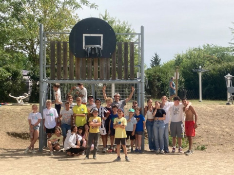 Een grote groep kinderen en tieners poseert voor een basketbalring bij Camping Le Château in Frankrijk.