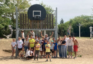 Un grande gruppo di ragazzi posa davanti a un canestro da basket al Camping Le Château, in Francia.