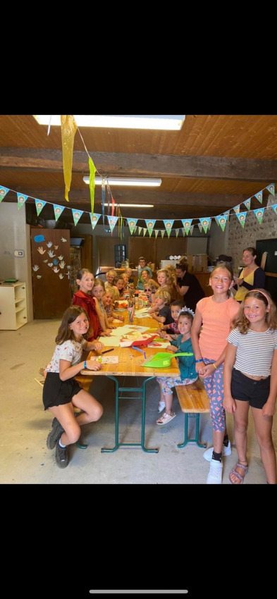 Kinder basteln gemeinsam an einem langen Tisch in einem bunt geschmückten Raum auf Camping Le Château.