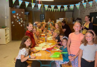 Children gather around a decorated table for arts and crafts inside the hall at Camping Le Château, France.