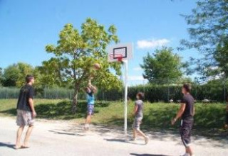 Four people playing outdoor basketball under sunny skies at Camping Le Château, Auvergne-Rhône-Alpes, France.