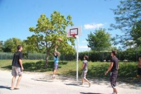 Cuatro personas juegan baloncesto al aire libre en un día soleado en Camping Le Château, Auvergne-Rhône-Alpes, Francia.