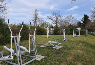 Outdoor gym equipment on a grassy lawn at Camping Le Château holiday park in Auvergne-Rhône-Alpes, France.