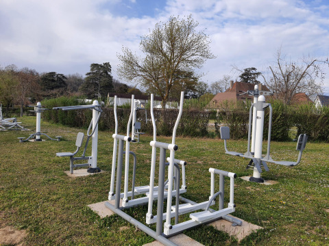 Équipements de fitness extérieurs installés sur la pelouse du Camping Le Château, avec maisons et arbres autour.