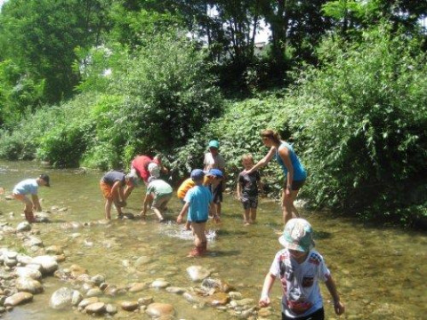 Kinder spielen im flachen Fluss bei Camping Le Château, umgeben von grüner Natur in Auvergne-Rhône-Alpes, Frankreich.