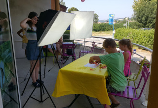 Kids doing crafts at a yellow-covered table with lighting at Camping Le Château, Auvergne-Rhône-Alpes, France.