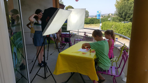 Kids doing crafts at a yellow-covered table with lighting at Camping Le Château, Auvergne-Rhône-Alpes, France.