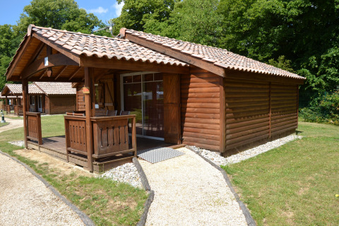 Bungalow in legno con veranda coperta al Camping Le Château, immerso nel verde in Auvergne-Rhône-Alpes.