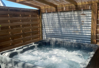 Spa privado junto a una caravana Airstream americana en Camping Le Château, Francia, bajo pérgola de madera.