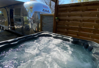 American Airstream caravan with private spa beneath pergola at Camping Le Château in France.