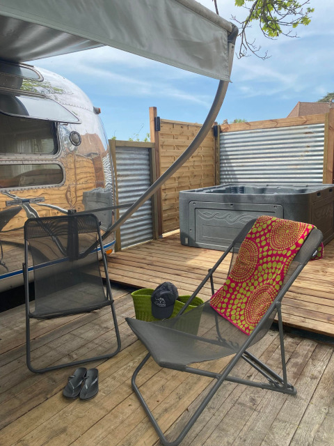 Terrasse mit Stühlen, Whirlpool und Airstream-Wohnwagen bei Camping Le Château in Frankreich.