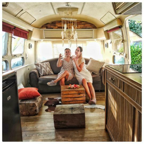 Twee vrouwen genieten van drankjes in een Amerikaanse Airstream-caravan met privéspa op een Franse camping.