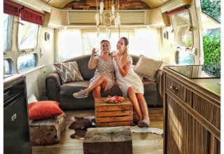 Due donne si rilassano con un drink in una roulotte American Airstream con spa privata in un campeggio in Francia.