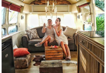 Due donne si rilassano con un drink in una roulotte American Airstream con spa privata in un campeggio in Francia.