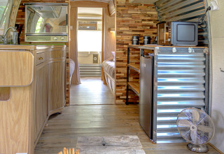 Interior de caravana American Airstream con spa privado y mobiliario de madera en Camping Le Château, Francia.