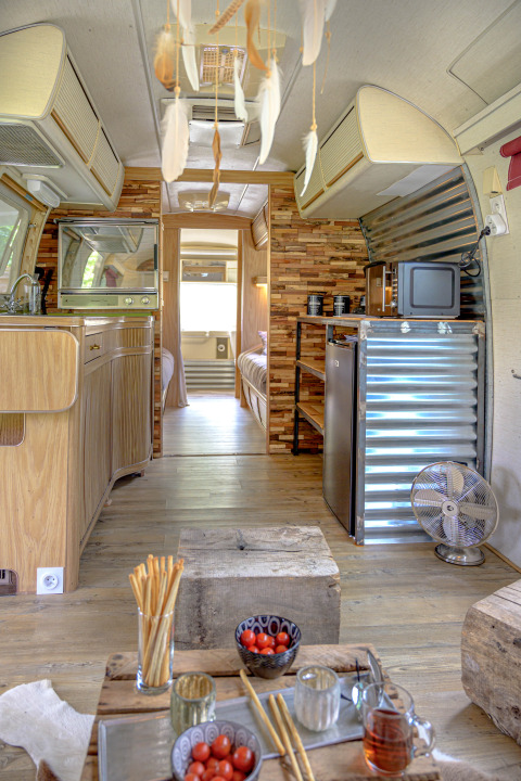 Interior de caravana American Airstream con spa privado y mobiliario de madera en Camping Le Château, Francia.