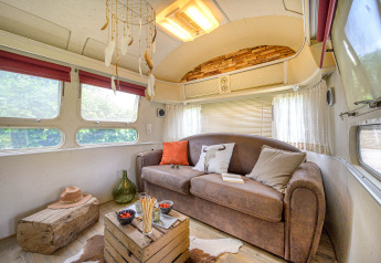 Cozy interior of an American Airstream caravan with sofa, rustic decor, and natural light at French campsite.